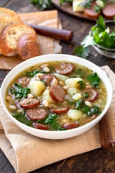 a bowl of soup with sausage, potatoes and spinach on a napkin next to bread