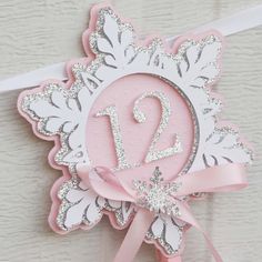 a pink and white birthday card with the number sixteen in it's center, hanging from a ribbon