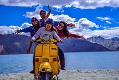 group of people riding on the back of a yellow scooter at the beach