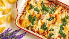 a casserole dish with cheese and spinach on it next to purple flowers