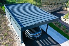 a car is parked under a metal structure in the driveway next to a garden area