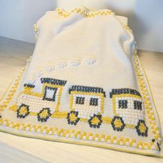 a crocheted baby blanket with yellow and black trains on the front, sitting on a wooden floor