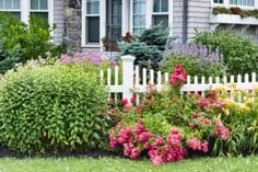 a white picket fence surrounded by flowers in front of a house