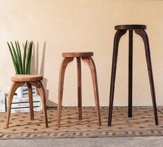 three wooden stools sitting next to each other in front of a wall and potted plant