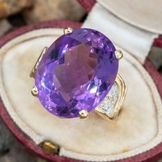 This amethyst cocktail ring is centered with one (1) oval mixed cut natural amethyst set into a four-prong setting. The shoulders of the ring are each accented with five (5), bead set, round brilliant cut diamonds. The ring measures 20.0mm at the top, rises 12.1mm above the finger, tapering to 3.3mm wide and 0.9mm thick at the base of the shank. The ring is currently a size 5. Formal Lavender Amethyst Ring With Oval Shape, Formal Lavender Oval Amethyst Ring, Formal Lavender Oval Ring, Oval Amethyst Ring With Gemstone Accents For Formal Occasions, Oval Amethyst Gemstones For Formal Occasions, Oval Amethyst Ring With Gemstone Accents, Oval Purple Amethyst Ring With Gemstone Accents, Formal Oval Amethyst Gemstones, Oval Purple Amethyst Ring With Center Stone