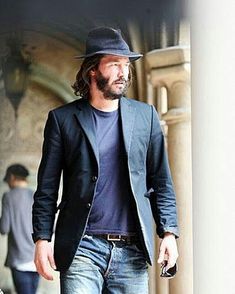 a man with a hat is walking down the street wearing jeans and a blazer