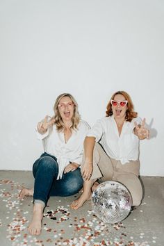 two women sitting on the floor with their hands in the air and some coins scattered around them