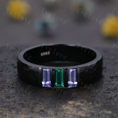 a black ring with three emeralds on it sitting on top of a stone surface