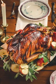 a roasted turkey on a platter with apples and other holiday foods around the table