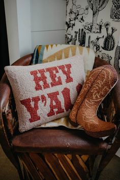 a pair of boots sitting on top of a brown chair next to a pillow that says hey yay