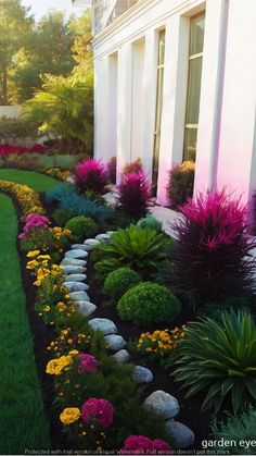 an outdoor garden with flowers and rocks in the grass next to a white house on a sunny day