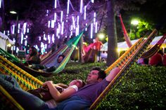 two men laying in hammocks at night with lights on the trees behind them