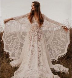 a woman standing in a field wearing a white dress with an intricate lace cape over her shoulders