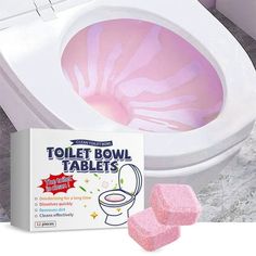 the toilet bowl is pink and has two sponges in front of it, next to a box of toilet paper