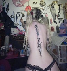 a woman with tattoos on her back standing in front of a wall