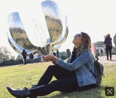 a woman sitting on the ground in front of a large metal object