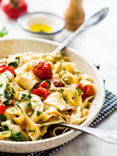 a white bowl filled with pasta and tomatoes on top of a blue checkered cloth