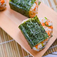 three sushi rolls on a wooden plate with rice and green toppings, sitting on a bamboo mat