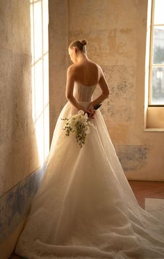 a woman in a wedding dress standing by a window