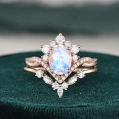 a white opal and diamond ring sitting on top of a green velvet cushioned surface