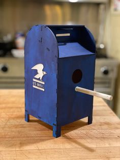 a blue mailbox sitting on top of a wooden table next to a white stick