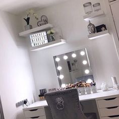 a white vanity with lights on it and a chair in front of the mirror that is lit up