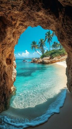 the view from inside a cave looking out at the ocean and beach with palm trees