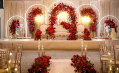 a decorated wedding stage with red flowers and greenery on the side, surrounded by candles