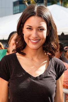 a woman standing in front of a crowd with her hand on her hip and smiling at the camera