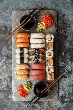 an assortment of sushi on a stone platter with chopsticks and sauce