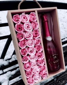 a box with pink roses and a bottle in it sitting on a wooden bench covered in snow