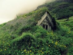 an old house on the side of a hill covered in grass and wildflowers