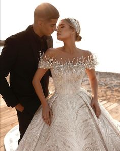 a man and woman standing next to each other wearing wedding dresses with beading on the shoulders