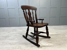 a wooden rocking chair sitting on top of a white table next to a gray wall