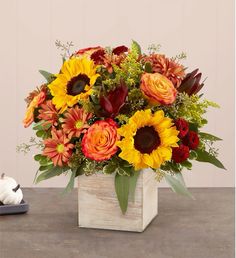 a bouquet of sunflowers and other flowers in a wooden vase on a table