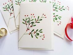 three cards with red berries and green leaves on them, next to some ribbon and scissors