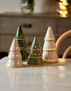 three ceramic christmas trees sitting on top of a white table next to a wooden chair