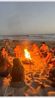 a group of people sitting around a campfire on the beach