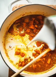 a pot full of stew being stirred with a whisk by a wooden spoon