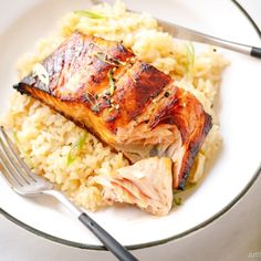 a white plate topped with meat and rice next to a fork on top of a table