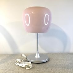 a pink table lamp sitting on top of a gray floor next to a white wall