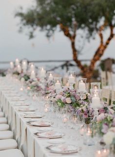 a long table is set up with white and purple flowers, candles and place settings