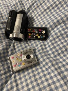 two cameras sitting on top of a blue and white checkered bed spread next to each other