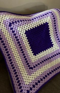 a purple and white crocheted blanket sitting on top of a couch next to a pillow