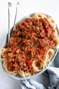 a plate of spaghetti with meat sauce and two silver spoons