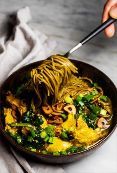 someone is eating noodles with broccoli and mushrooms in a bowl on the table