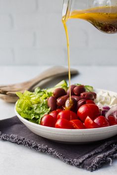 olives, tomatoes and lettuce are being poured into a bowl with dressing