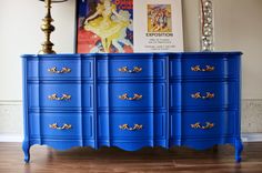 a blue dresser sitting on top of a hard wood floor next to a lamp and pictures