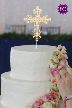 a close up of a person cutting a cake with a cross on top and flowers around it