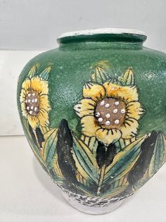 a green vase with sunflowers painted on the outside and inside, sitting on a white surface